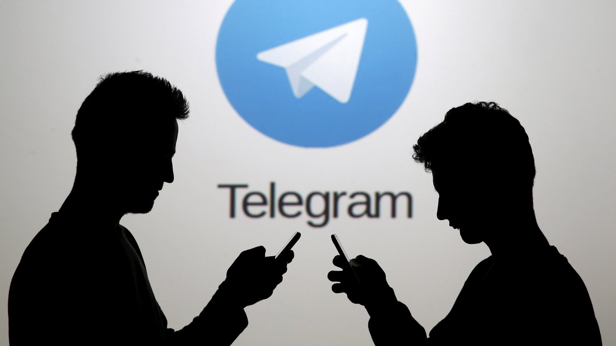 FILE PHOTO: Men pose with smartphones in front of a screen showing the Telegram logo in this picture illustration
